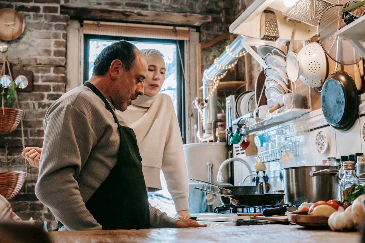 Concentrated middle aged ethnic man in apron and woman standing together in kitchen during dinner preparation at home